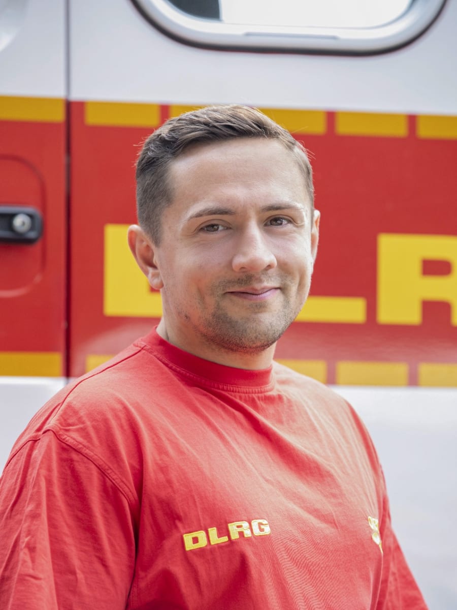 Dennis Faulhaber in DLRG-Kleidung vor einem Einsatzfahrzeug